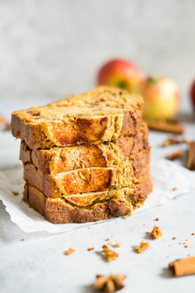 Slices of cinnamon apple bread recipe, some scrambled around and some apples and fall spices on the background.