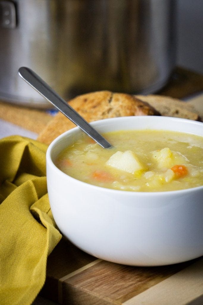 Scottish Potato Soup and Tattie Soup Recipe in a bowl with bread and potatoes beside and soup pot in the background