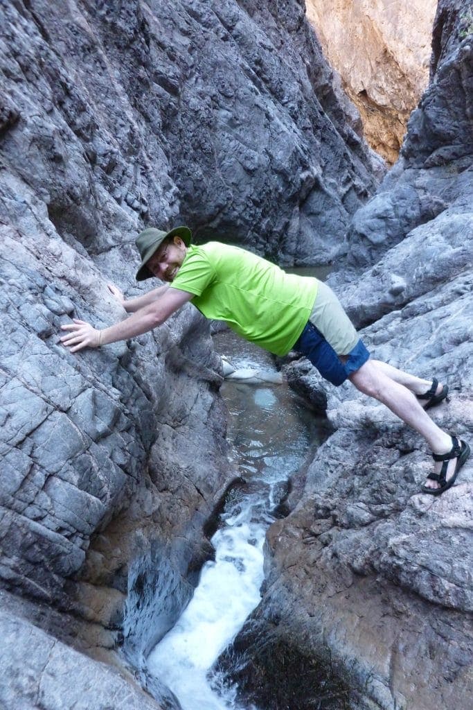 Dan makes a human bridge with his feet on one cliff edge of the slot canyon and his hands on the other. White water gushes through the slot below.