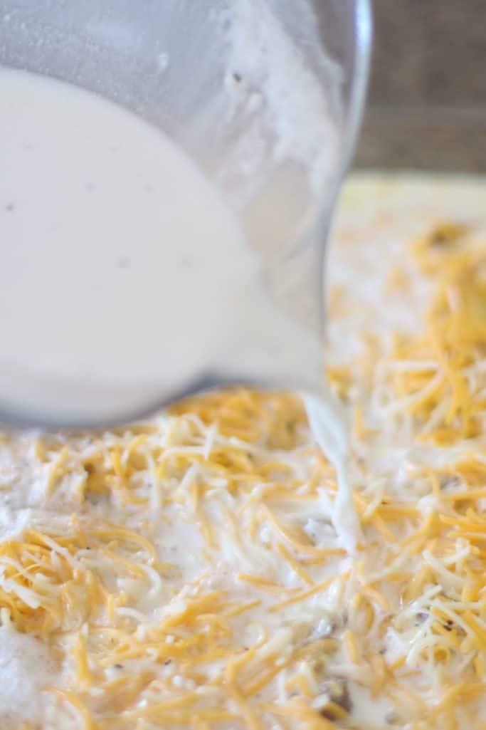 prepared gravy mixture pouring over biscuits, sausage and shredded cheddar cheese
