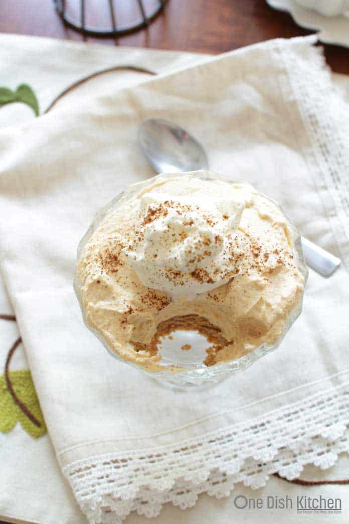 Overhead view of a spoonful missing from Pumpkin Cheesecake in dessert glass on a white cloth napkin