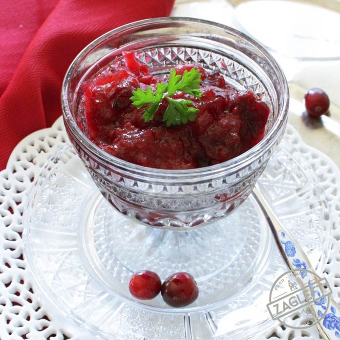 Cranberry sauce in a dessert glass plated on a metal tray with scattered cranberries and a spoon