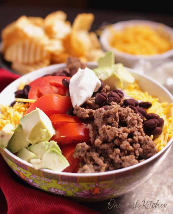 a closeup photo of a taco salad served in a bowl topped with sour cream | one dish kitchen