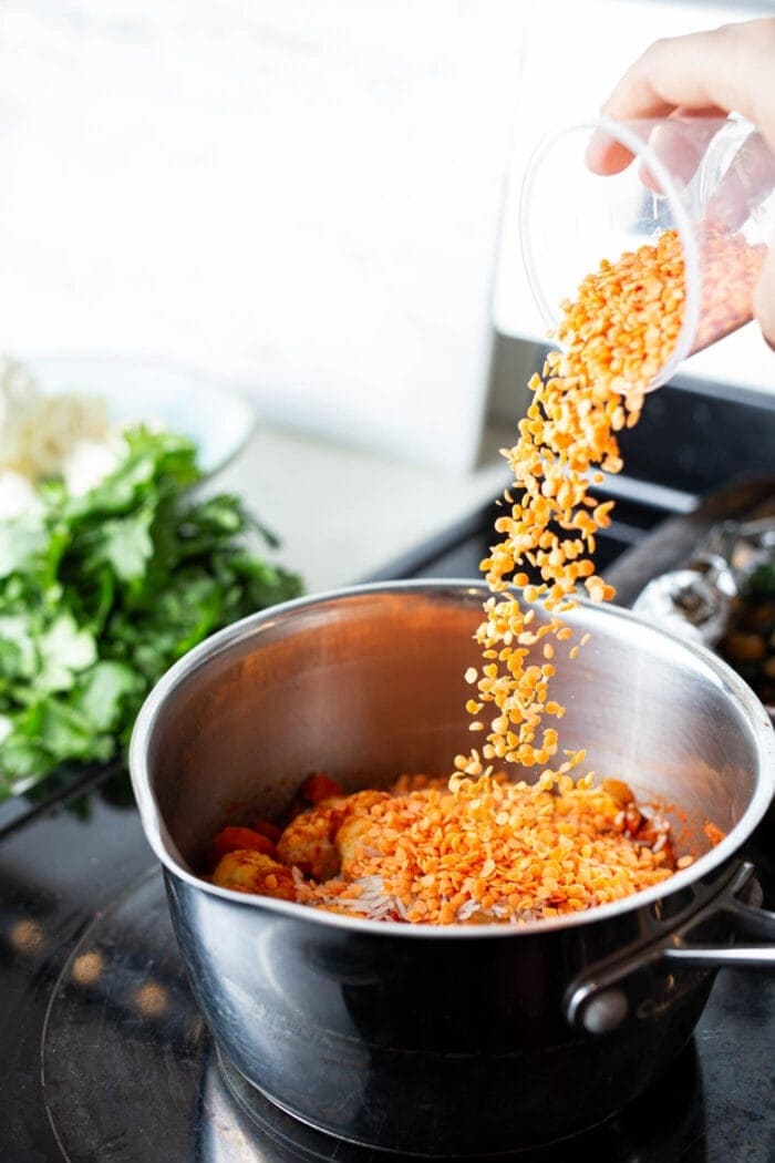 Adding red lentils to a pot of cauliflower curry stew.