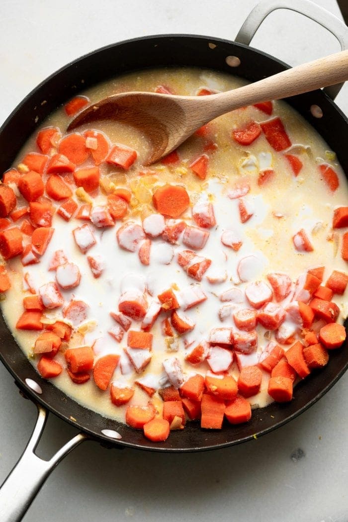 Cooking carrots, coconut milk, vegetable broth and onions for vegan coconut ginger carrot soup.