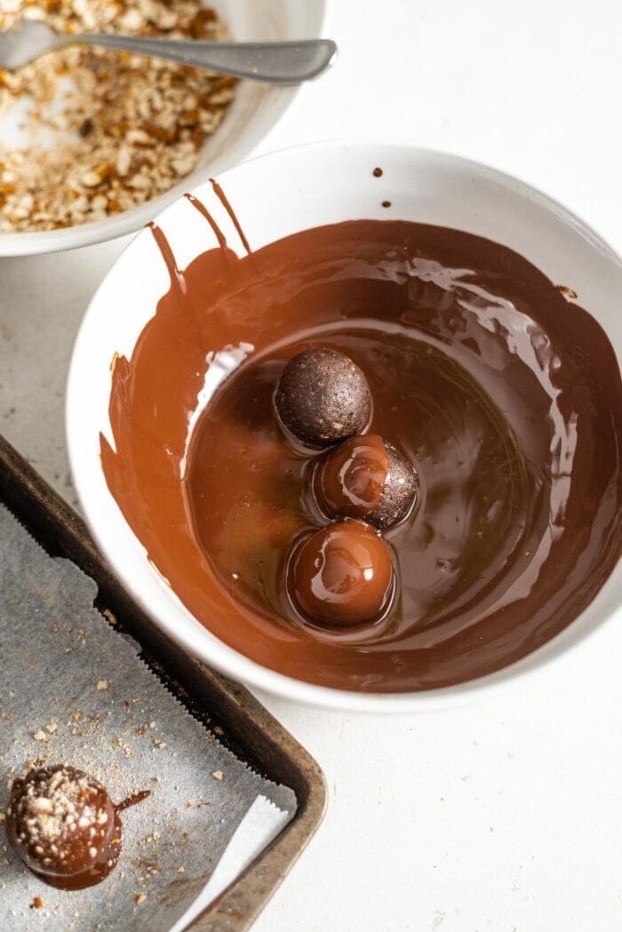 3 chocolate truffles in a bowl of melted chocolate.