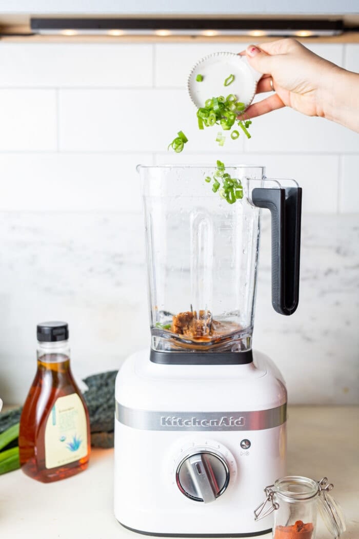 Adding chopped green onions to a blender to make miso peanut sauce.