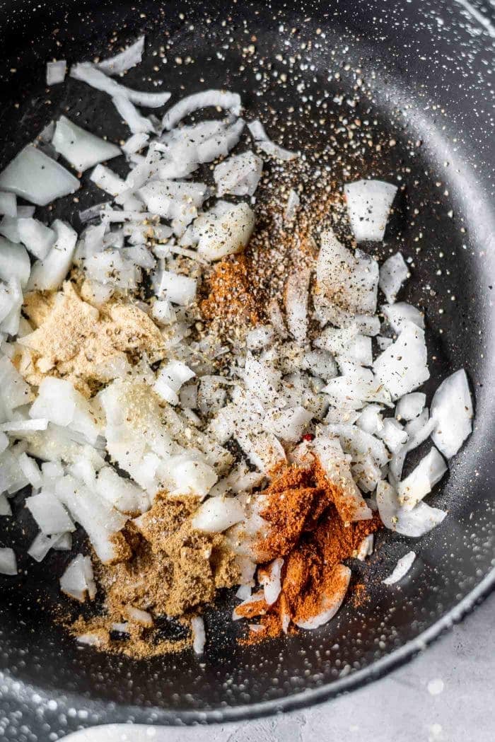 Diced onions and taco seasonings in a black skillet.