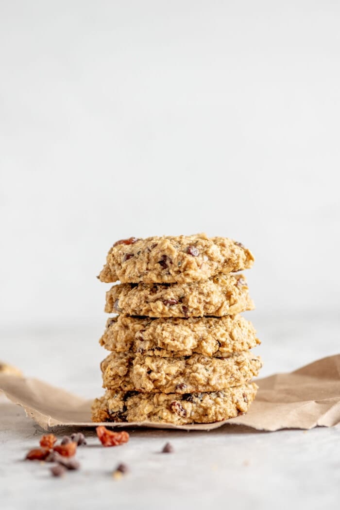A stack of vegan and gluten-free, healthy oat cookies sitting on brown paper with some raisins scattered around.
