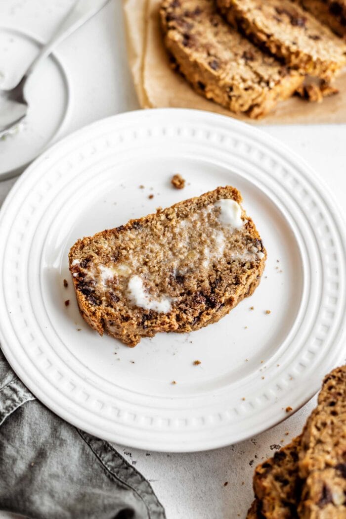A sliced of chocolate chip banana bread slathered with butter.