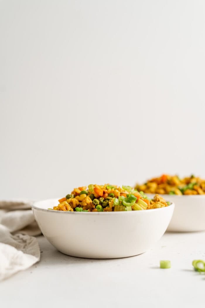 Two bowls of vegan fried brown rice with a few pieces of green onion scattered around.