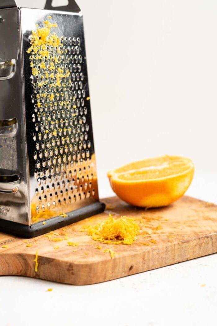 Orange zest, a box grater and a half a sliced navel orange sitting on a chopping board.