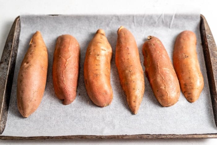 6 medium-sized sweet potato halves placed face down on a baking tray lined with parchment paper.