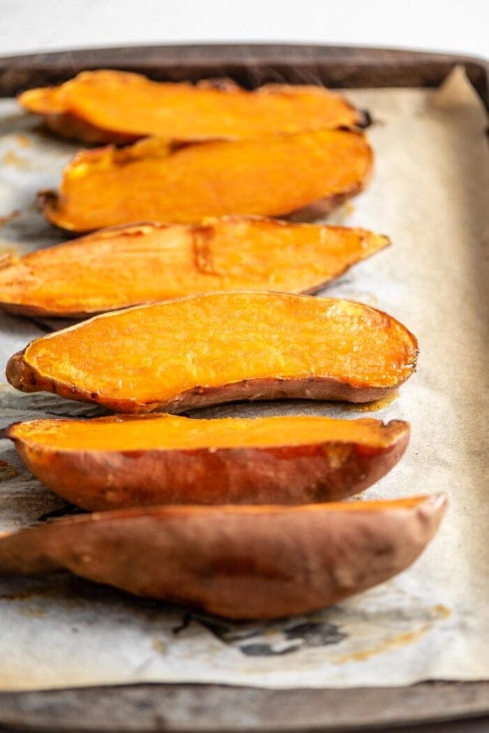 6 baked sweet potato halves on a baking tray lined with parchment paper.