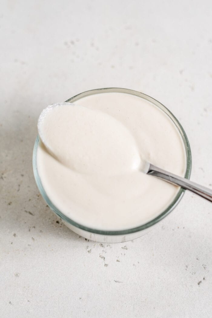 A spoon in a small glass dish of cashew cream.
