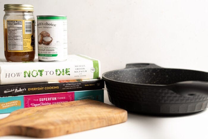 Cutting board, black frying pan and a stack of books with 2 cans of food top of them.