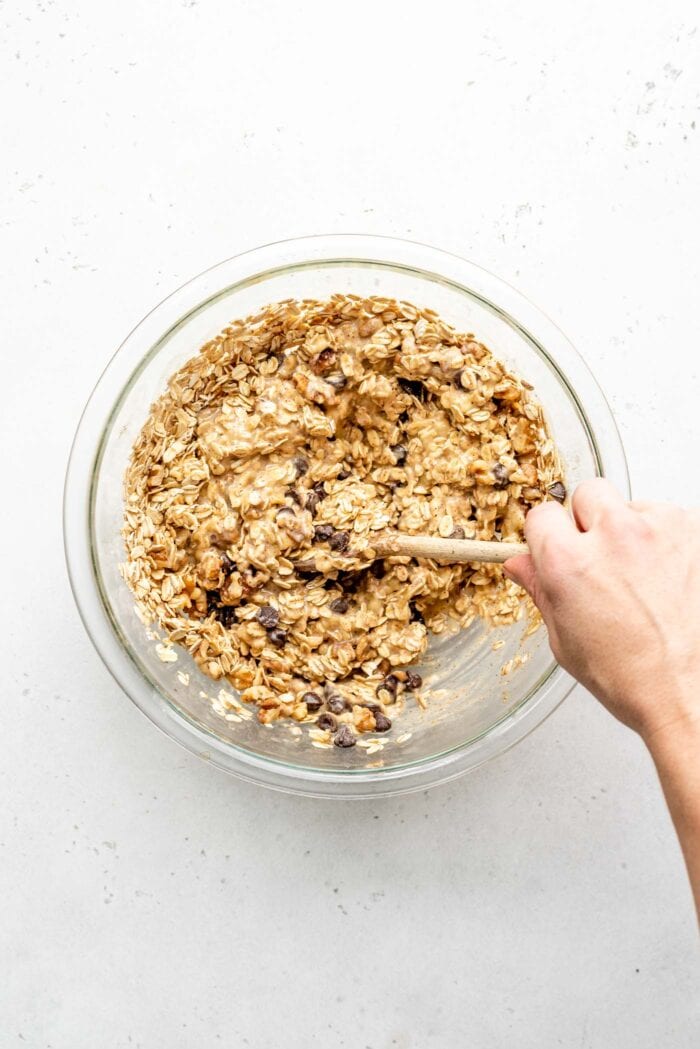 Raw banana oatmeal cup dough in a mixing bowl with a wooden spoon.