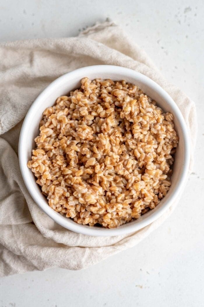Cooked farro in a bowl sitting on top of a dish cloth.