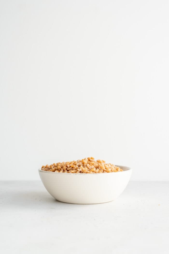 A bowl of cooked farro sitting on a white surface.