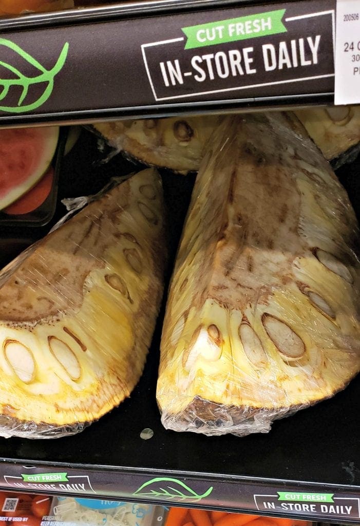 1/8th of a jackfruit is packaged in plastic wrap and sits on a shelf in produce