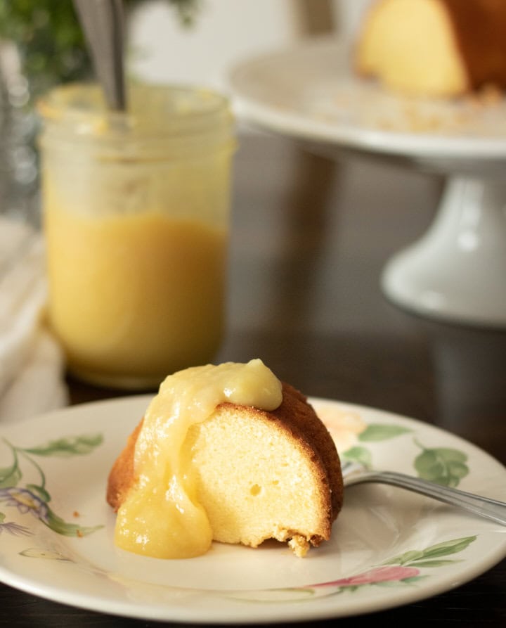 big chunk of pound cake with cake on stand in background and lemon curd topping
