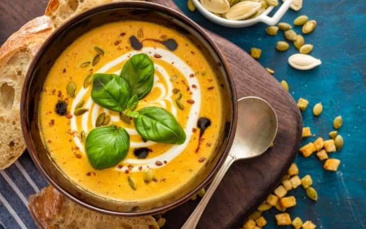 pumpkin soup with basil garnish resting on a wooden cutting board with a slice of rustic bread beside it making it one of the perfect fall soup recipes
