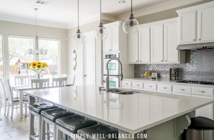 An all white decluttered minimalist kitchen with a large island.