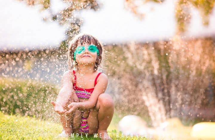 Little girl playing in backyard sprinkler