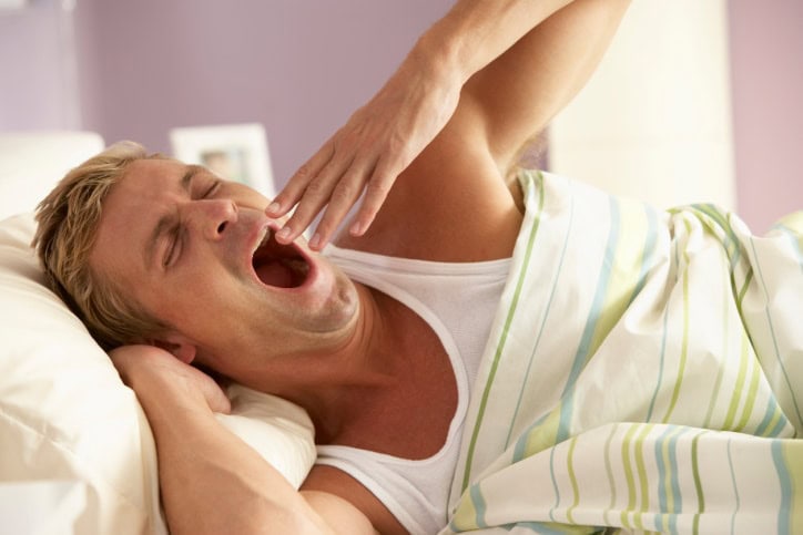 A guy is yawning in the bed