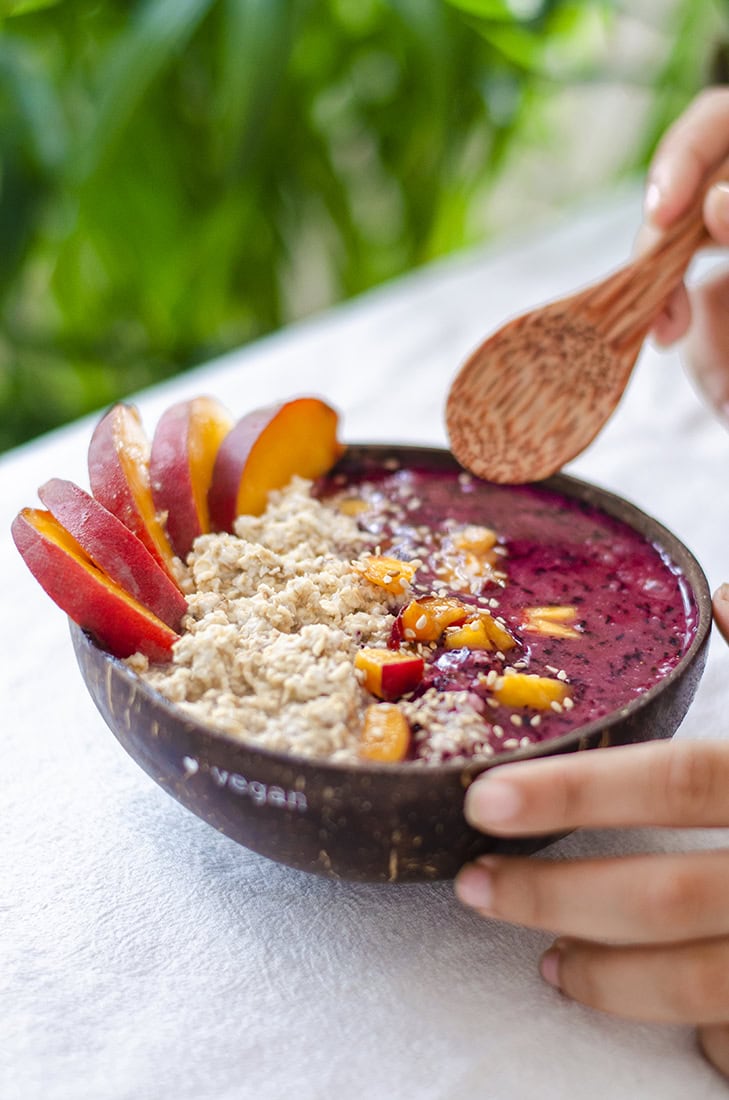 Coconut bowl de avena y helado casero de arándanos con rodajas de melocotón. Un desayuno vegano fácil, rápido y barato.