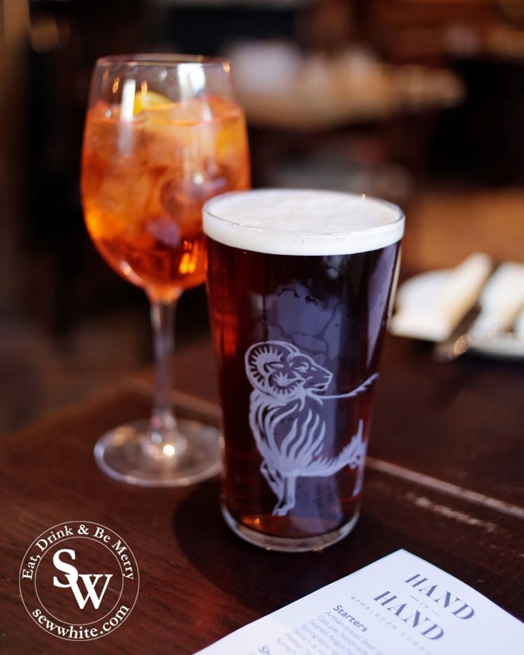 A youngs brewery ram on a glass at The Hand in Hand in Wimbledon Village with an Aperol Spritz in the background.