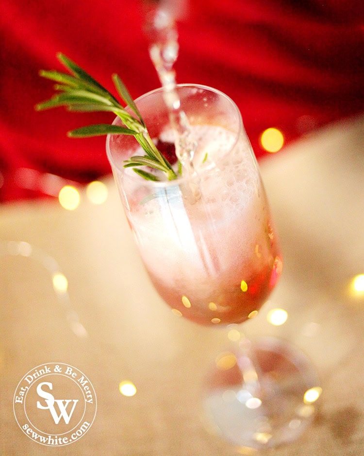 Pouring the Prosecco over the raspberry liqueur making the rosemary and fresh cranberries bubble up for the Raspberry Rosemary Fizz