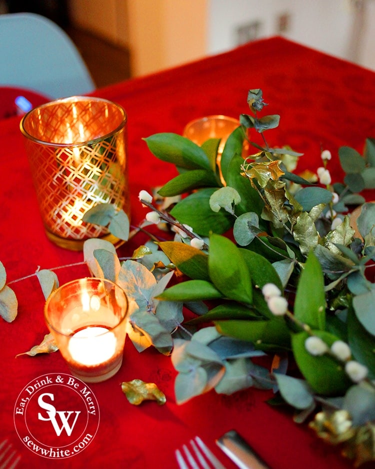 Christmas table with red table cloth and fresh greenery studded with golden candles.