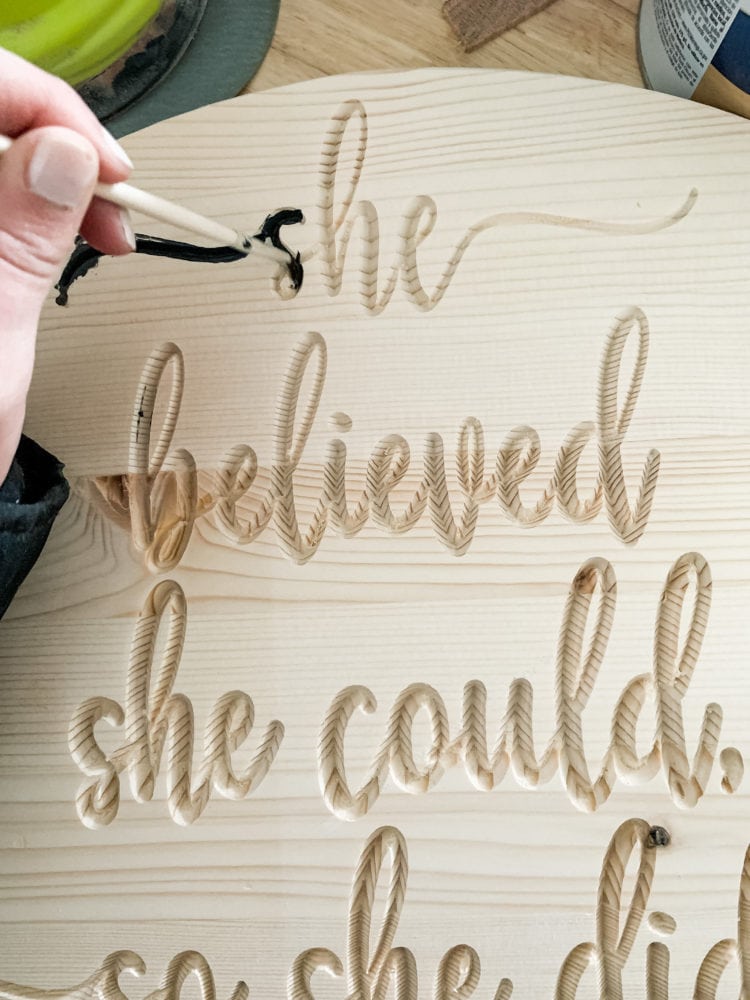 woman's hand painting detailed letters on a wood carved sign