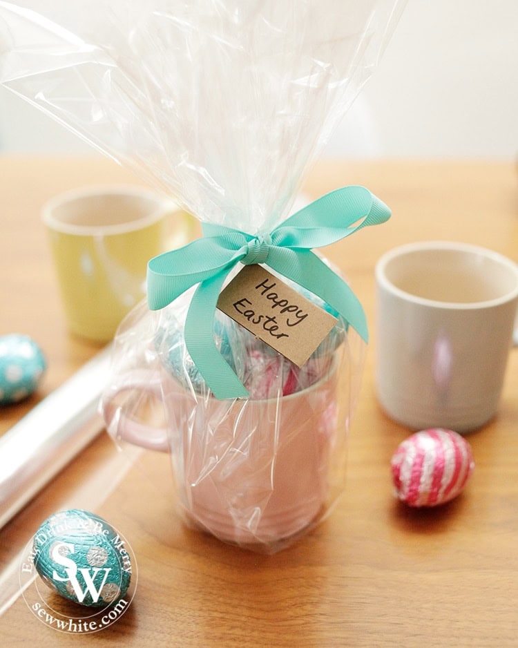 wrapping up a mug filled with easter eggs and wrapped up with clear film and a ribbon.