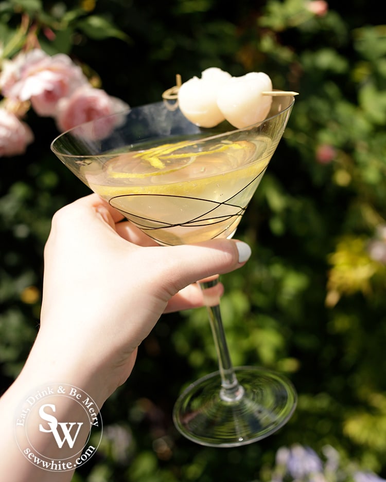 Cheers to a beautiful cocktail. Large cocktail glass being held against roses with lychees in it.