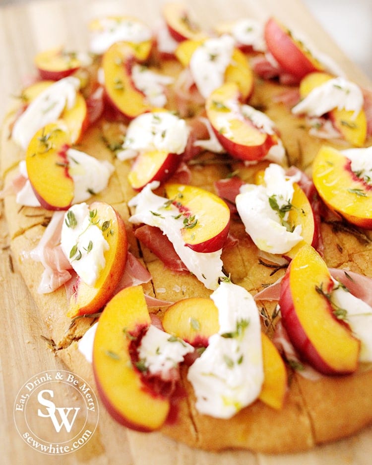 Homemade golden Focaccia cut up into pieces topped up with parma ham, peach slices, mozzarella and decorated with thyme and drizzled with olive oil. Easy Party Bites.