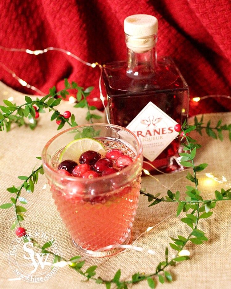 Sparkling Cranberry Ginger Cocktail made with Cranes cranberry liqueur decorated with fresh cranberries and a slice of lime. Christmas cocktail