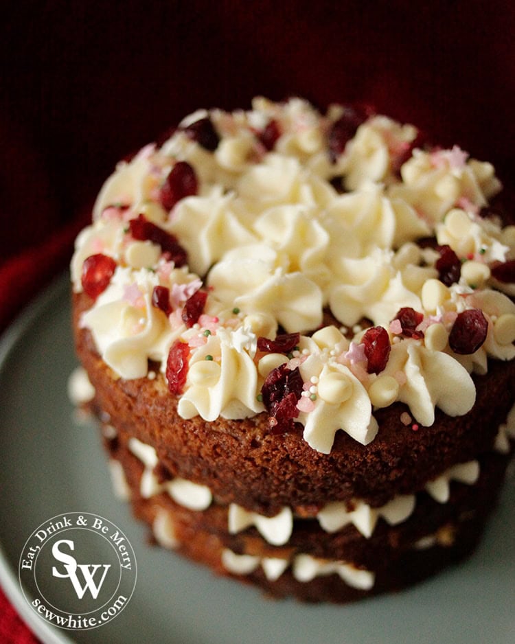 Three tiered golden brown white chocolate and cranberry cake decorated with buttercream swirls, dried cranberries and white chocolate chips. Plus pink star sprinkles.