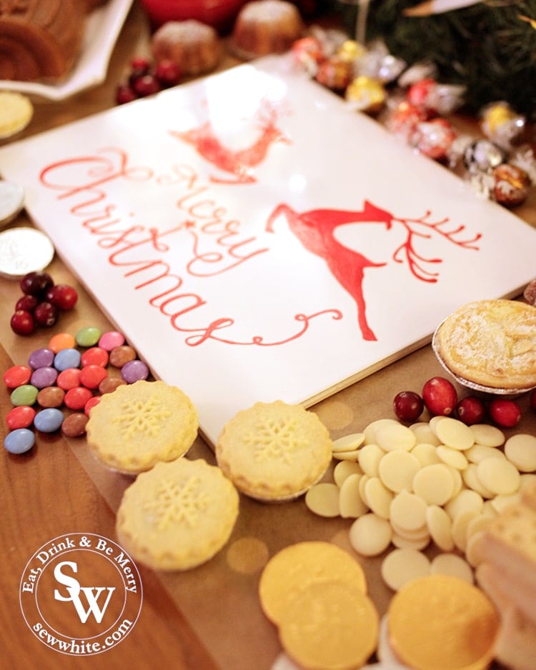 Close up of mince pies, chocolate buttons, fresh cranberries and smarties with a merry christmas sign.