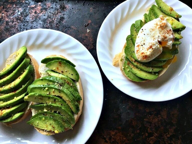 overhead shot of three avocado toasts, one plate with an avocado toast with poached egg on top and the others with sliced avocado only