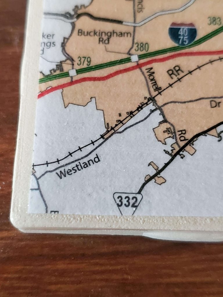 Corner of a DIY map coaster, showing border of tile and map cut out.