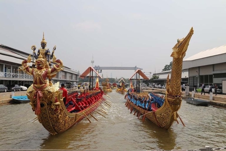 Two gilded long boats sit in river facing camera. One has swan-shaped, tall bow. The other has two creatures, one on top of the other.