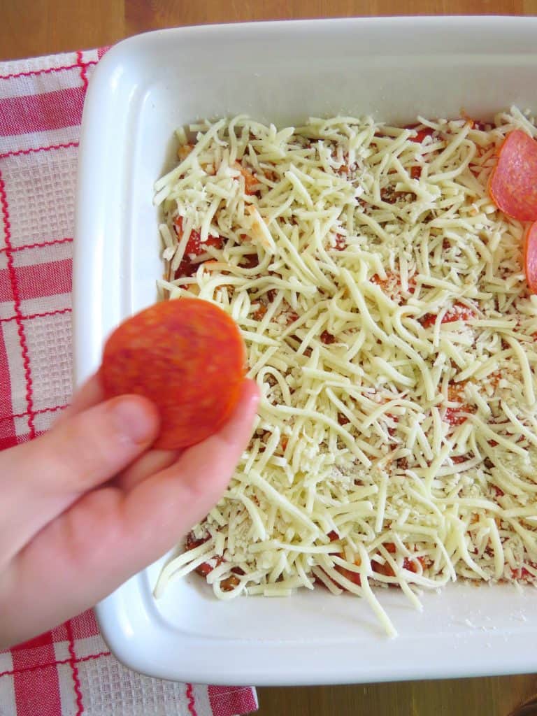 Alex adding pepperoni slices to bubble up pizza casserole