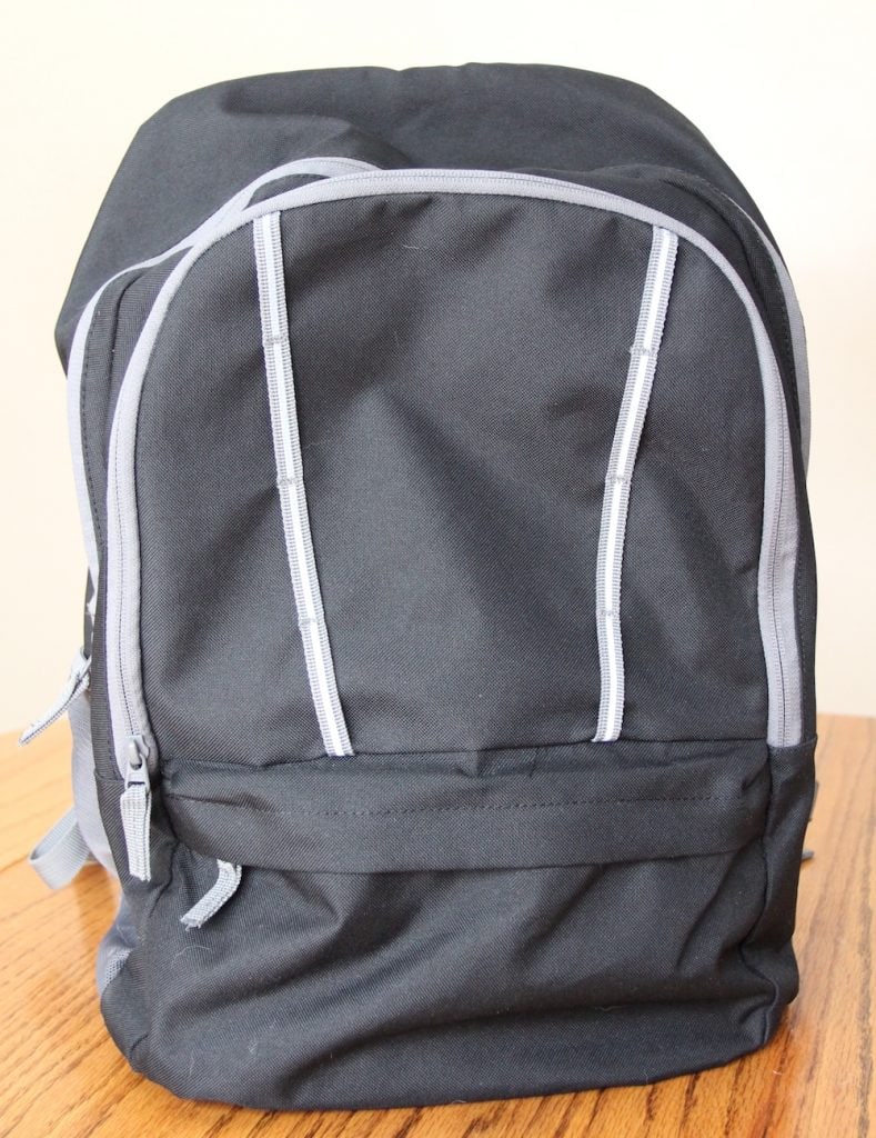 Black backpack zipped up and ready to go home, sitting on a table.