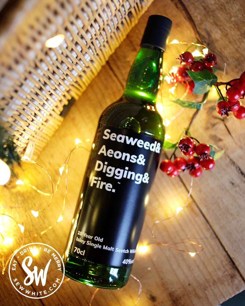 Seaweed & Aeons & Digging & Fire single malt bottle in the drink gift guide lying on a table with lights around it
