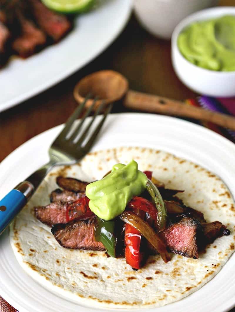 A plate of food on a table, with grilled steak fajitas and guacamole