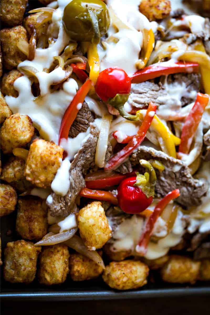 A dish is filled with food, with Cheesesteak, tater tots, and cheese