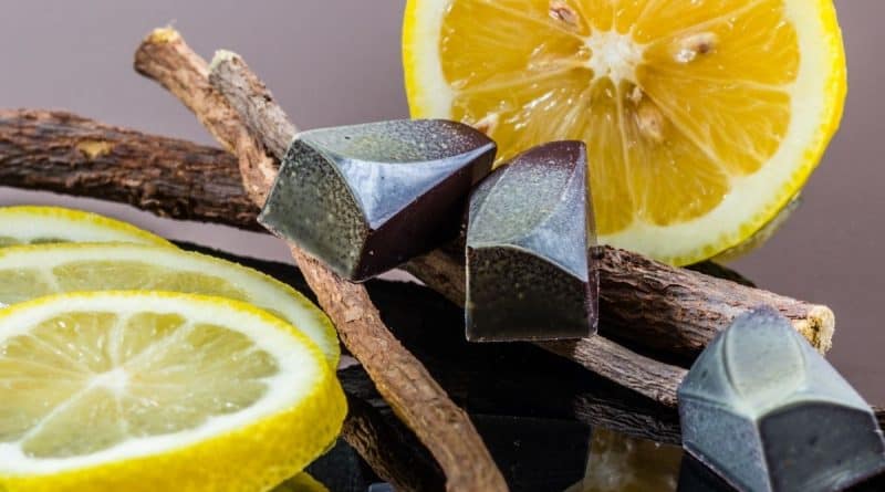 Black licorice candies sitting on licorice root, with lemon slices behind.