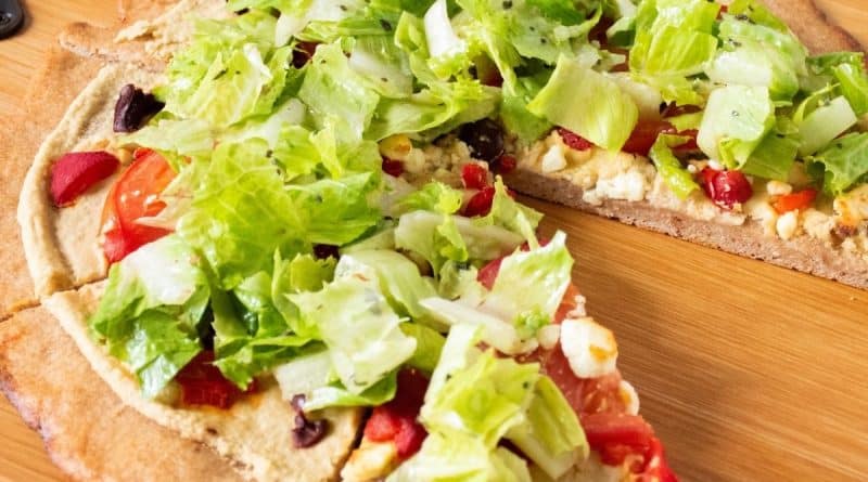 Pizza on a peel, with whole wheat crust, topped with salad.